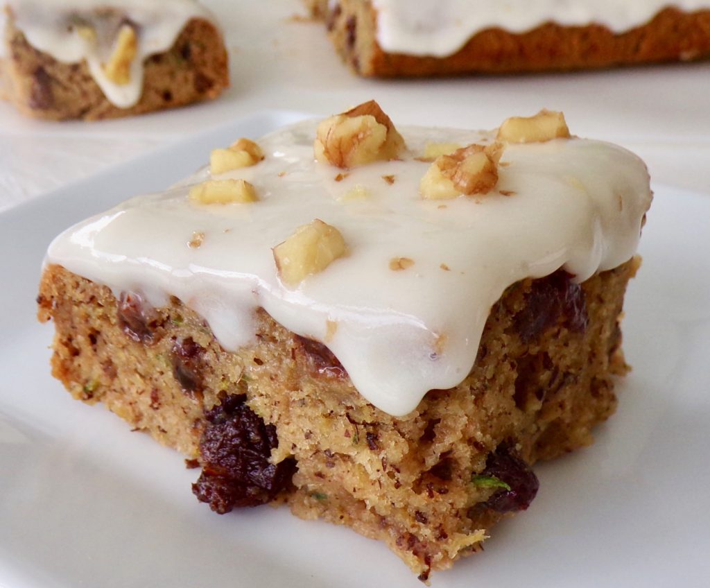 slice of vegan zucchini cake with cream cheese frosting and walnuts