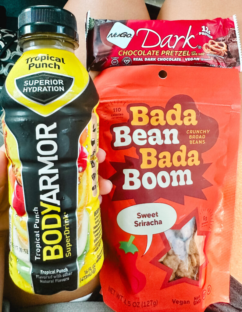 assortment of vegan snacks: savory broad beans, sweet protein bar, and body armor electrolyte drink